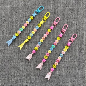 May include: Five colorful beaded keychains with smiley face charms and star accents. Each keychain has a different color scheme and a different word spelled out in gold letters.