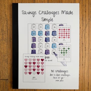 May include: A white notebook titled "Savings Challenges Made Simple" with illustrations of shopping bags, hearts, and piggy banks. The notebook includes text about saving £100 to £400 with 30 challenges.