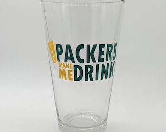 May include: A clear glass with a green and yellow design that says "Packers Make Me Drink".