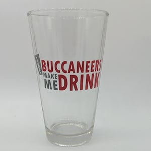 Puede incluir: Un vaso de vidrio transparente con el texto "The Buccaneers Make Me Drink" impreso en rojo y gris en el lateral.