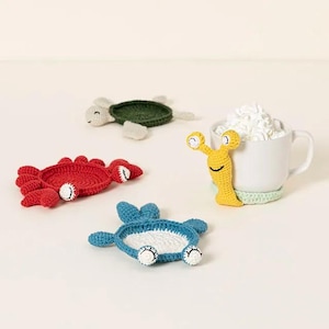 May include: Four crocheted animal coasters in the shapes of a crab, turtle, snail, and a starfish. The coasters are red, green, yellow, and blue.