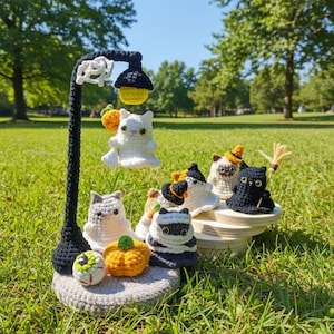 Può includere: Un'eccentrica esposizione di Halloween all'uncinetto con un lampione nero con luce gialla, un gatto fantasma bianco e vari gatti all'uncinetto, zucche e un bulbo oculare. L'esposizione è ambientata su una base all'uncinetto grigia e una piattaforma di legno.