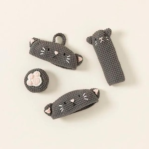 May include: Set of four gray crocheted cat-shaped toys. Two of the toys are headbands with cat faces and ears. One toy is a small, round cat paw. The fourth toy is a long, thin cat with a face and ears.