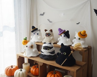 May include: A collection of handmade crochet Halloween cat figures, each with unique hats and accessories. The cats are white, black, and tan, with some resembling ghosts or mummies. Pumpkins and candles decorate the wooden display.