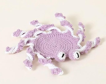 May include: A crocheted purple and white octopus with large eyes. The octopus is made of soft yarn and has a textured surface.
