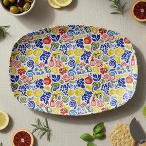 May include: Oval serving platter with a colorful Italian-themed design. The white platter features a repeating pattern of grapes, tomatoes, lemons, and bottles in red, blue, yellow, and green. The words "ITALIA APERITIVO" are also printed on the platter.