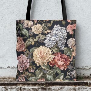May include: A tote bag with a floral design. The bag has a dark background with flowers in pink, yellow, and white. The bag has black handles. The bag's dimensions are not visible.