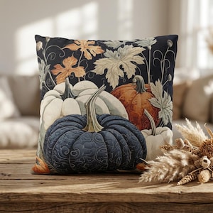 May include: A square throw pillow featuring a dark navy blue background with a printed pattern of pumpkins in shades of white, orange, and dark blue, accented by light-colored autumn leaves and thin, winding vine illustrations across the fabric.