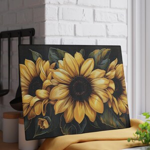 May include: A rectangular glass cutting board featuring a vibrant illustration of three large yellow sunflowers with dark brown centers, surrounded by deep green leaves against a solid black background, creating a high-contrast floral design.