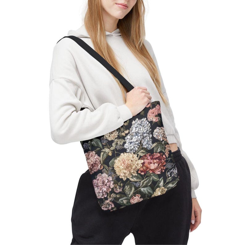 May include: Black tote bag with a floral pattern featuring pink, cream, and blue flowers. The bag has a black shoulder strap and is made of a sturdy fabric. The floral design is set against a dark background.