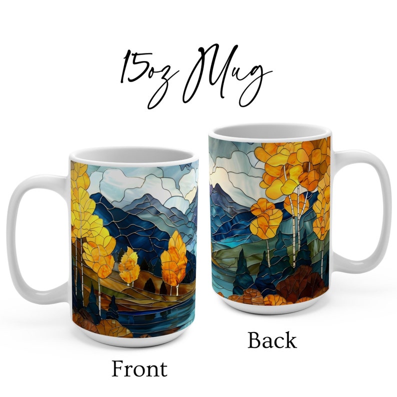 May include: White ceramic 15oz mug with a stained glass design of a mountain landscape with yellow trees and a blue lake. The front of the mug shows a close-up of the trees and lake, while the back shows a wider view of the mountain landscape.