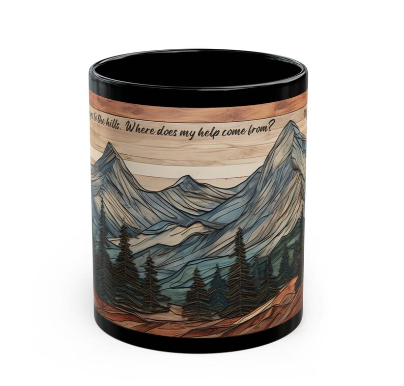 May include: A black ceramic mug featuring a wrap-around graphic of layered mountain peaks and pine trees over a wood-grain background. The text "I lift up my eyes to the hills. Where does my help come from?" is printed in black script near the top rim.