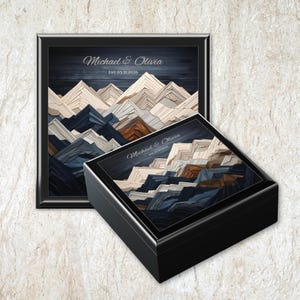 May include: A black framed art print and a black box featuring a mountain landscape design in shades of blue, brown, and white. The text "Michael & Olivia" and the date "05.31.2026" are displayed on both items.