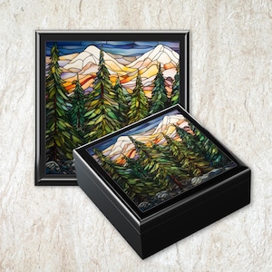 May include: A square black box and a matching framed wall art piece, both featuring a stained glass style illustration of a mountain range with snow-capped peaks behind a dense forest of green pine trees under a dark blue sky.