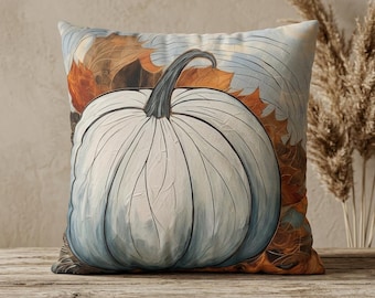 May include: A square throw pillow featuring a large, pale blue pumpkin with a dark stem centered on the front. The background displays a detailed illustration of layered autumn leaves in shades of orange, brown, and tan with soft blue accents.