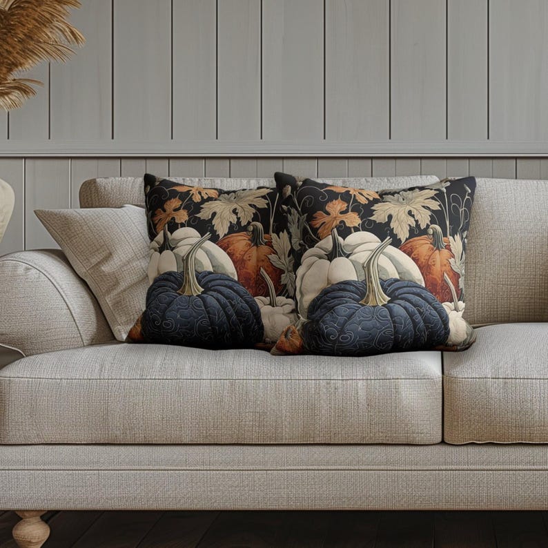May include: Two square throw pillows featuring a dark background with a repeating pattern of orange, white, and dark blue pumpkins, along with light-colored autumn leaves. The pillows have a quilted texture and are placed side by side on a sofa.
