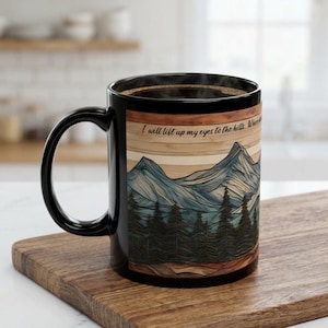 May include: A black ceramic mug featuring a wrap-around graphic of a mountain range and pine forest. The design includes a light wood-grain texture background and the printed text, I will lift up my eyes to the hills. Where does my help come from?