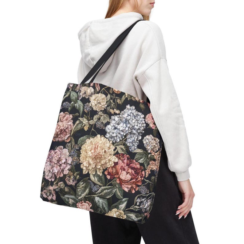May include: A black tote bag with a floral design featuring pink, yellow, and white flowers. The bag has a black strap and is carried over the shoulder. The floral design is set against a dark background.