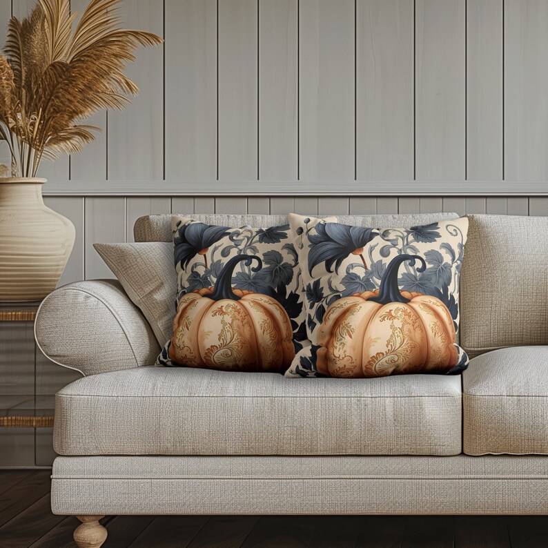 May include: Two square throw pillows featuring a detailed orange pumpkin illustration with intricate gold filigree patterns. The background of the pillows displays a dark blue botanical leaf motif on a cream-colored fabric base.