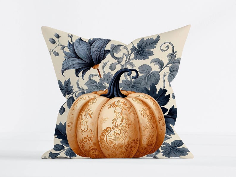 May include: A square throw pillow featuring a central orange pumpkin with intricate gold filigree patterns. The background displays a cream-colored fabric printed with dark blue botanical illustrations of large flowers and leafy vines.