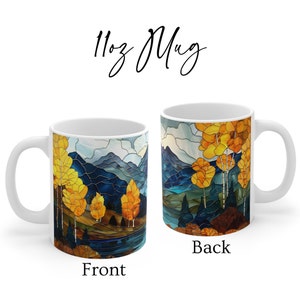 May include: White ceramic mug with a stained glass design of a mountain landscape with a lake and trees in autumn colors. The front of the mug shows a close-up of the trees and lake, while the back shows a wider view of the mountains. The mug is 11oz.