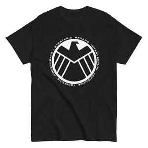 Può includere: Maglietta nera con una grafica bianca del logo S.H.I.E.L.D. Il logo è un cerchio con un falco al suo interno e il testo "Strategic Hazard Intervention Espionage Logistics Directorate".
