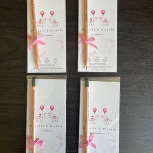 May include: Four white cards with pink and black illustrations of elephants holding balloons. Each card has a pink ribbon and a wooden pencil with a black eraser. The text on the cards reads "Manuela & Michela 9 Compleanno" and "Muela & Michela Compleanno".