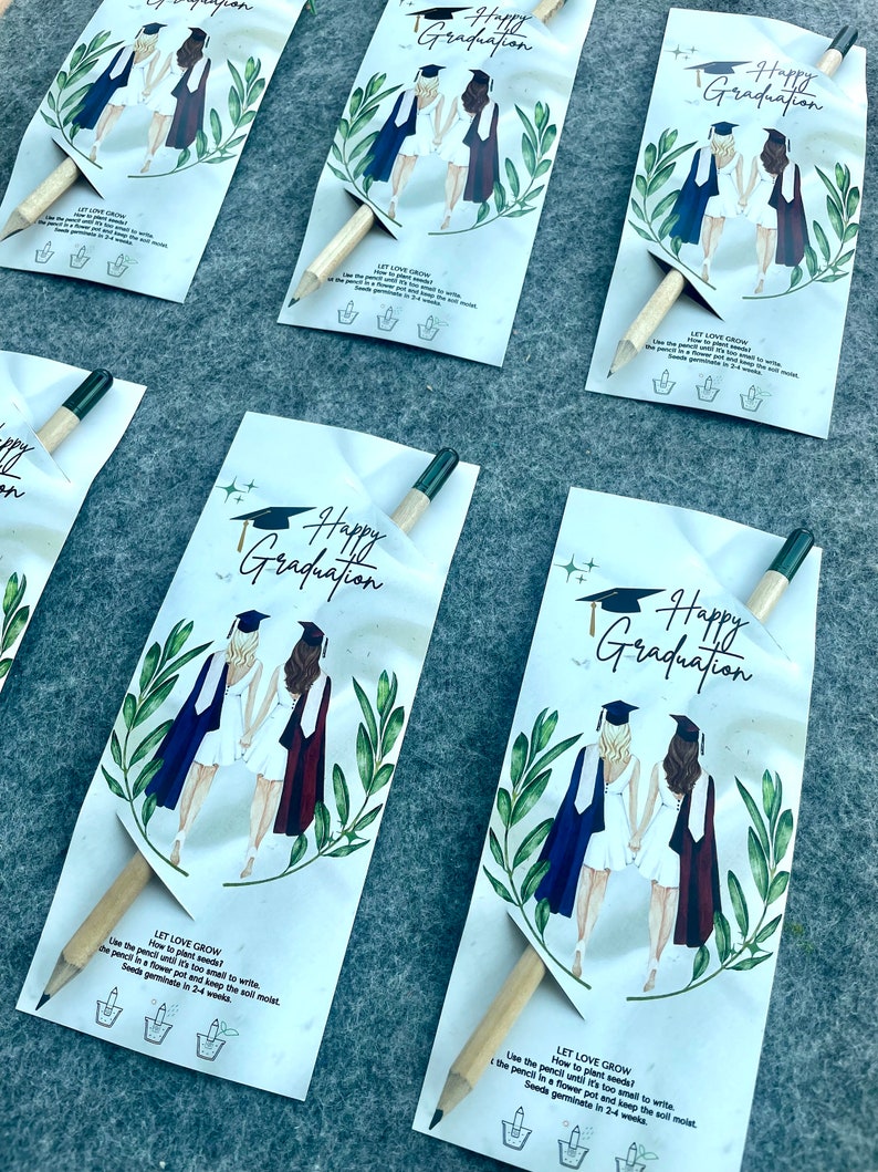 Może przedstawiać: Dwie postacie w togach w kolorze niebieskim i czerwonym, z czapkami absolwent&oacute;w, trzymające się za ręce przed zielonym, liściastym tłem. Obrazek znajduje się na białej kartce z tekstem "Happy Graduation" i instrukcjami, jak posadzić oł&oacute;wek, kt&oacute;ry jest oł&oacute;wkiem nasionowym.