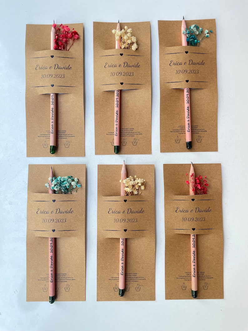 May include: Six brown cardstock favor boxes with pink pencils and dried flowers. Each box has the text "Erica & Davide" and "10.09.2023" printed on the front.