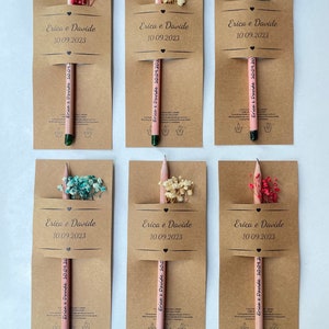 May include: Six kraft paper favor boxes with pink pencils and dried flowers. Each box has the text "Erica & Davide" and the date "10.09.2023".