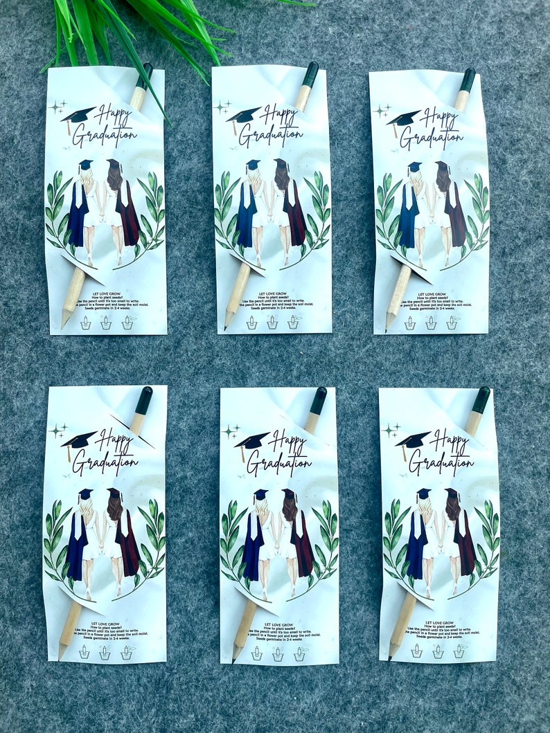 Może przedstawiać: Sześć białych kopert z papieru z oł&oacute;wkiem w środku każdej. Koperty mają zielony wz&oacute;r liści i rysunek dw&oacute;ch kobiet w togach absolwent&oacute;w. Tekst na kopertach brzmi "Happy Graduation".