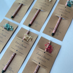 May include: A set of six brown paper favor bags with pencils and dried flowers. Each bag has a label with the text "Erica e Davide" and a date.