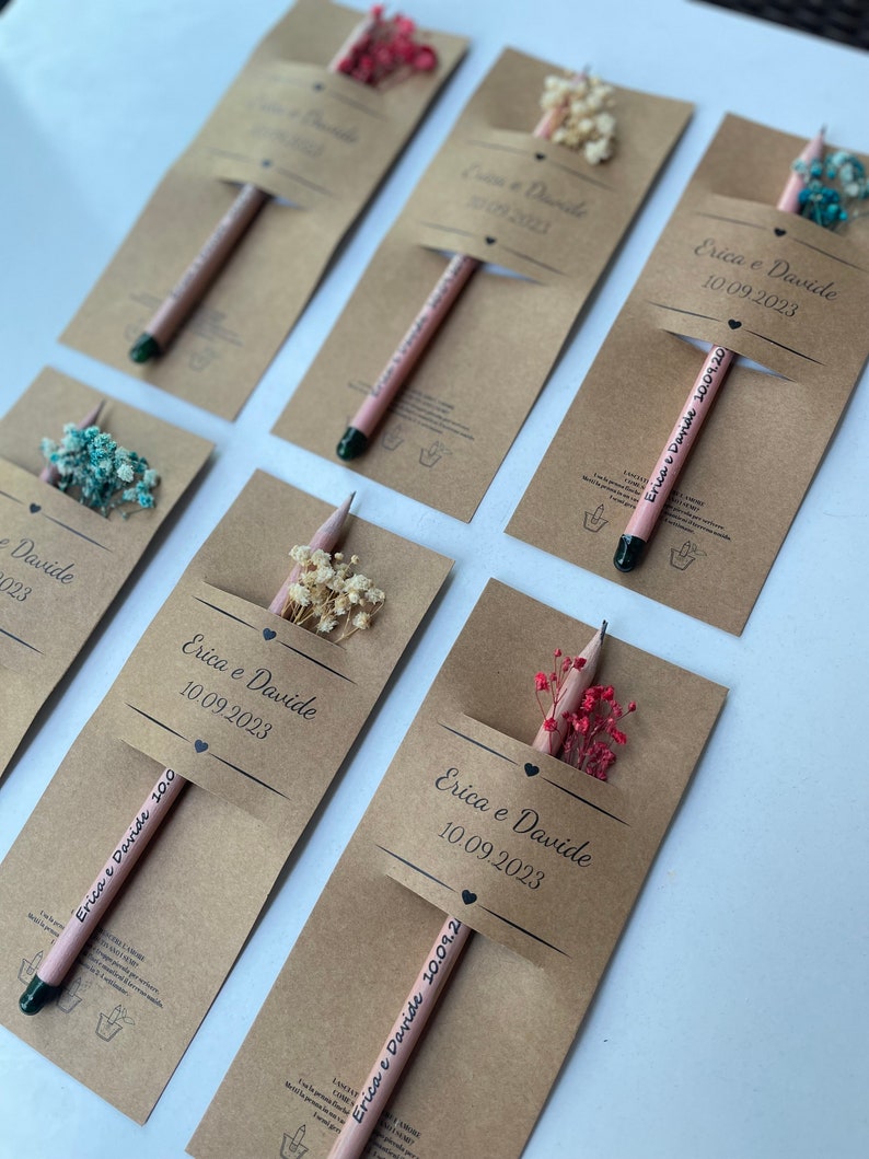 May include: A set of six brown paper favor bags with pencils and dried flowers. Each bag has a label with the text "Erica e Davide" and a date.