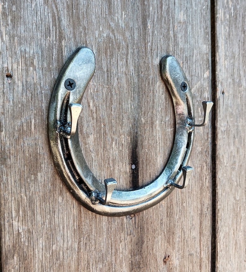 May include: A silver horseshoe-shaped coat rack with four hooks. The rack is mounted on a wooden wall.