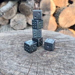 May include: A stack of six black metal dice with white dots on a wooden surface.