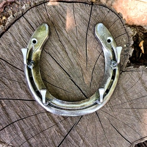 May include: A silver horseshoe with four nail hooks on a wooden surface.