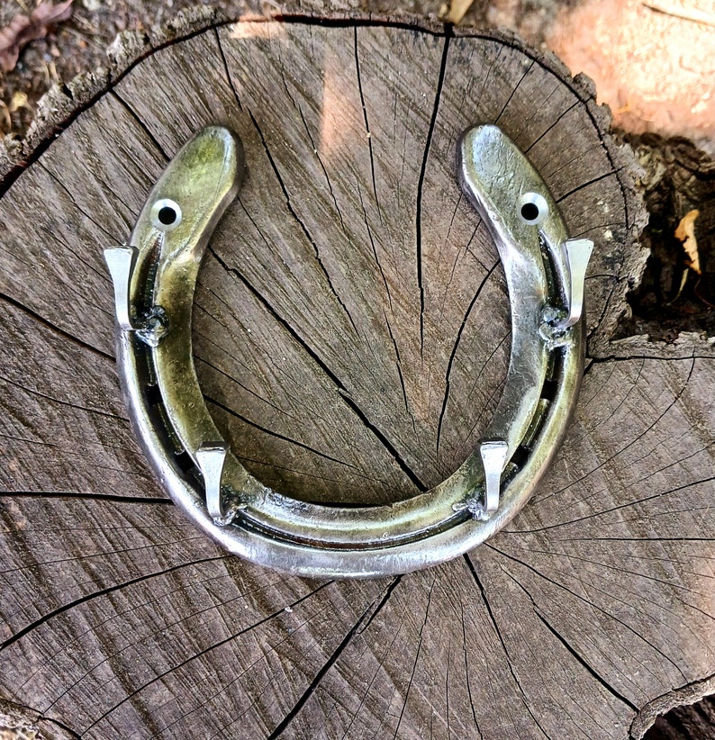 May include: A silver horseshoe with four nail hooks on a wooden surface.