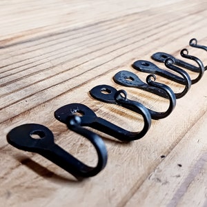 May include: A set of seven black metal hooks with a decorative swirl at the top of each hook. The hooks are arranged in a row on a wooden surface.