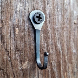 May include: A black metal hook with a screw head, mounted on a wooden surface.