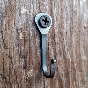 May include: A black metal hook with a screw head, mounted on a wooden surface.