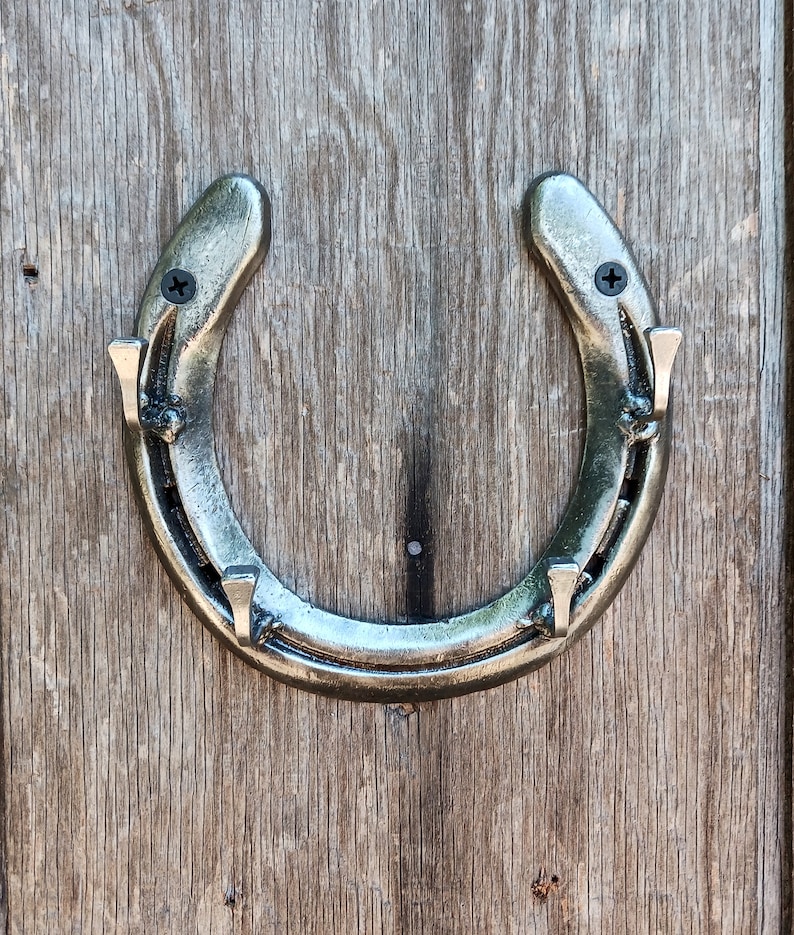 May include: A silver horseshoe-shaped coat rack with four hooks. The rack is mounted on a wooden wall.