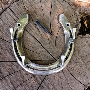 May include: A silver horseshoe with four hooks attached to it. The horseshoe is on a wooden surface.