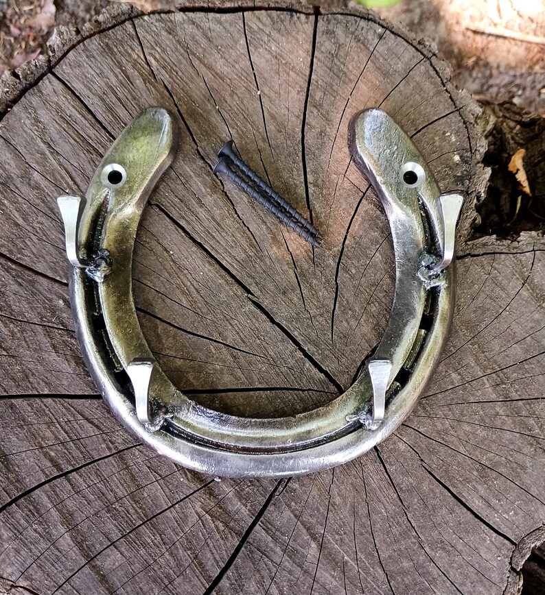 May include: A silver horseshoe with four hooks attached to it. The horseshoe is on a wooden surface.