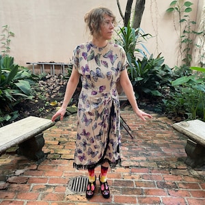 Vestido de crepé de seda con estampado de mariposas de los años 40, dobladillo con flecos, polisón lateral, borlas decorativas y cremallera metálica en la costura lateral y en el escote.