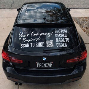 Könnte beinhalten: Ein schwarzes Auto mit weißen Aufklebern auf der Heckscheibe. Die Aufkleber lauten "Your Company, Business, Scan to Shop" und "Custom Decals Made to Order". Ein QR-Code ist ebenfalls sichtbar. Das Nummernschild lautet "PREMIVM."