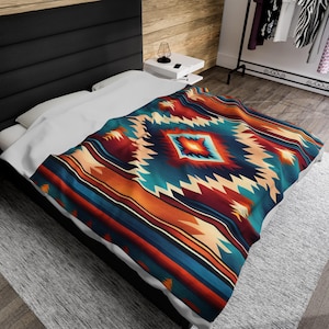 May include: A white bed with a colorful geometric patterned blanket. The blanket features a large diamond shape in the center with a turquoise, orange, and red color scheme. The blanket has a southwestern or Native American inspired design.
