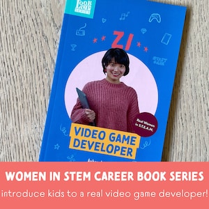 May include: A blue book cover with the title "ZI VIDEO GAME DEVELOPER" and a photo of a woman holding a tablet. The book is part of the "Women in STEM Career Book Series" and introduces kids to a real video game developer.