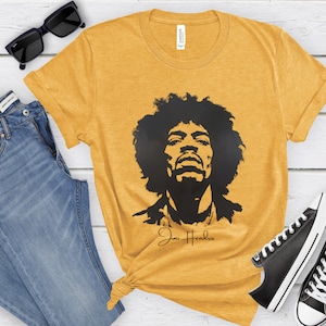 May include: A yellow t-shirt featuring a black silhouette of Jimi Hendrix and his signature in gold lettering.