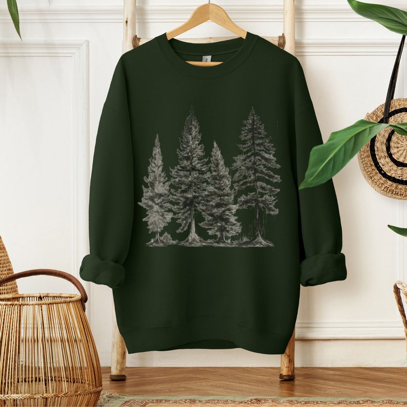 May include: A dark green sweatshirt with a graphic print of a forest scene featuring five trees. The trees are drawn in a simple, minimalist style with gray lines.