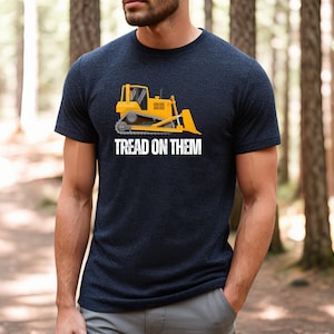 Może przedstawiać: Koszulka w kolorze granatowym z nadrukiem żółtego buldożera i tekstem "Tread on Them".